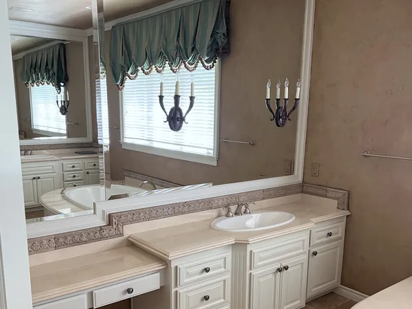 Before: dated white double vanity with a large mirror and wall sconces, Lake Sherwood