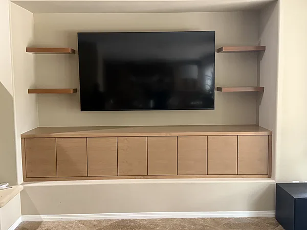 Light wood media console with floating shelves on both sides of a wall-mounted TV, Camarillo