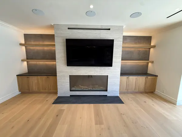 Fireplace media wall flanked by lit floating oak shelves over oak base cabinets, Thousand Oaks