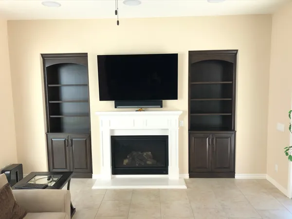 Dark stained arched bookcases on both sides of a white fireplace with a TV above, Moorpark