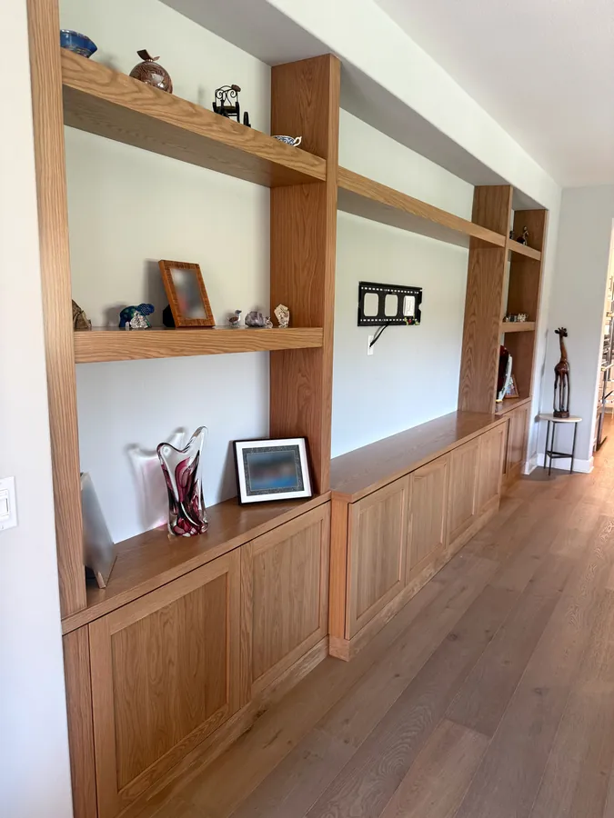 Long built-in wall of oak shelving over shaker base cabinets