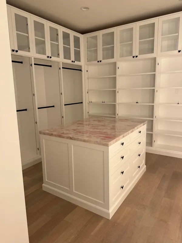 White walk-in closet with a center island, glass-front upper cabinets, hanging sections and shelving