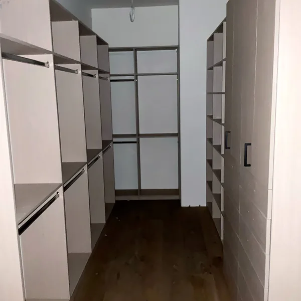 View down a walk-in closet aisle with hanging sections on both sides and a drawer bank