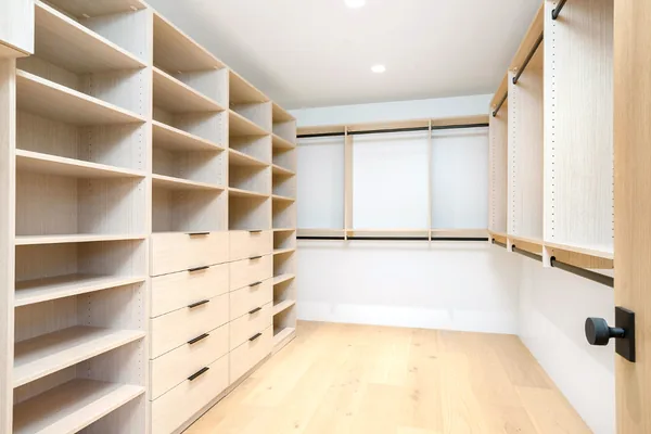 Bright walk-in closet with a light oak shelving wall, drawer bank and hanging rods on a wide plank floor