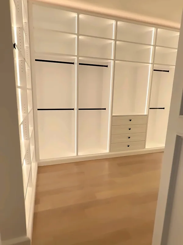 Walk-in closet with LED-lit open hanging sections, black rods and a center drawer stack