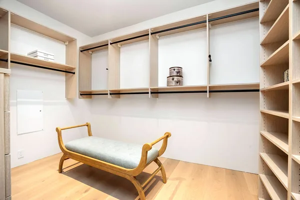 Bright walk-in closet with light oak shelving and hanging rods, upholstered bench in the center, Thousand Oaks