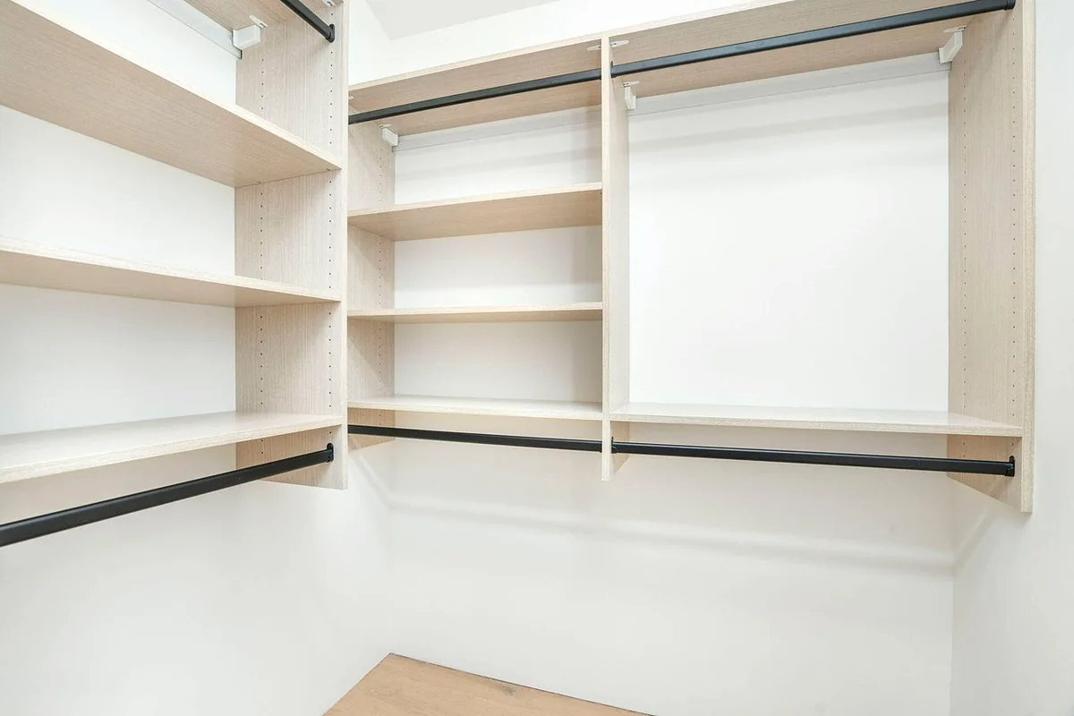 Corner of a closet with light oak open shelving and black double-hanging rods, Thousand Oaks