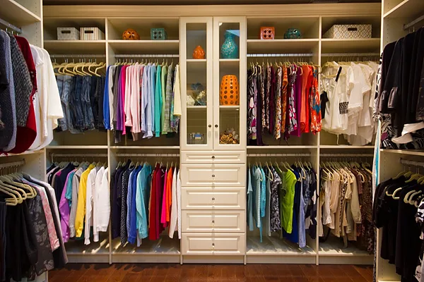 Walk-in closet wall with hanging sections and a center drawer tower with glass-front cabinets
