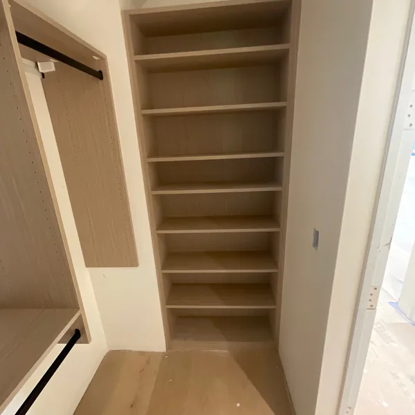 Reach-in closet shelf tower in a light wood finish beside a hanging rod