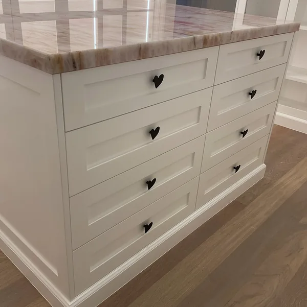 Closet island with white drawers, black hardware and a stone top