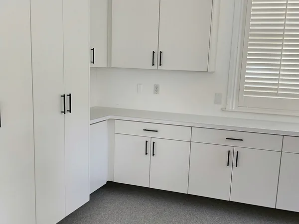 Tall white cabinets, wall cabinets and base cabinets with black pulls wrapping a garage corner, Hidden Hills
