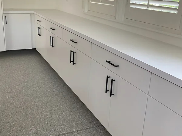 Long run of white garage base cabinets with black pulls and a white counter below shuttered windows, Hidden Hills