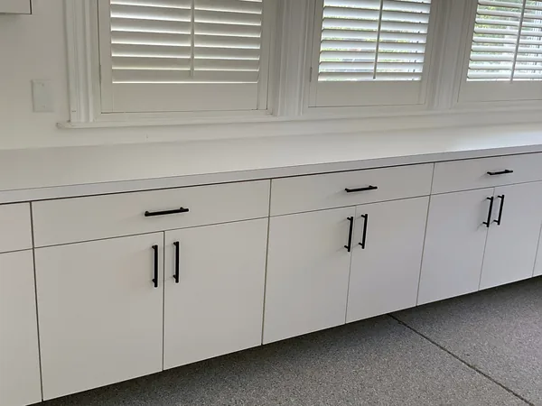 White garage base cabinets with black bar pulls and a long white counter under shuttered windows, Hidden Hills