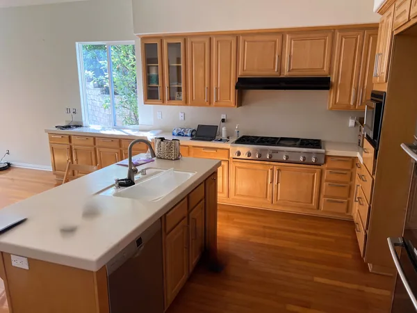 Warm wood kitchen cabinets around a large island with a white top, Thousand Oaks