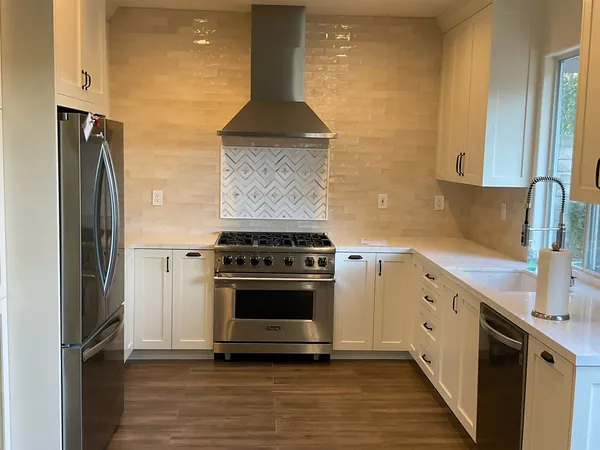 White shaker kitchen with a stainless range hood, tile backsplash and professional range in Newbury Park