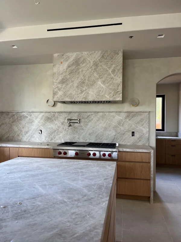 White oak slab kitchen with a marble island and a stone range wall with a hood