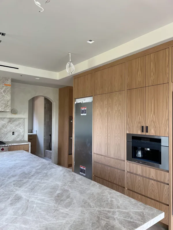 Wide marble island in front of a white oak appliance wall