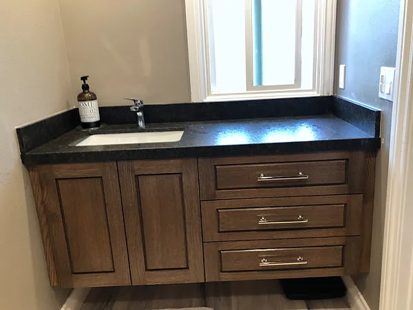 Stained wood vanity with drawers and a dark stone top below a window, Thousand Oaks