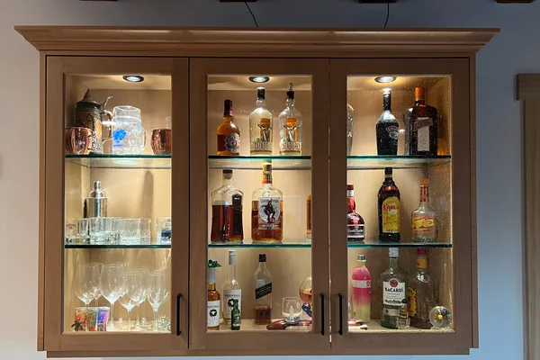 Wall-hung light oak bar cabinet with three glass doors, crown molding and lit glass shelves, Santa Rosa Valley