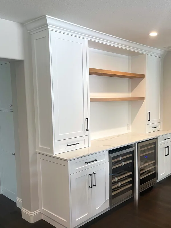 White shaker beverage center with two undercounter wine fridges, oak floating shelves and tall cabinets on each side